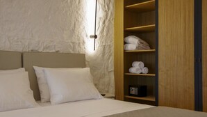 A bedroom with a bed, two pillows, a wooden wardrobe with towels, and a bedside table with a radio. - Villa Marenthe | 3 BDR | Sea Views | Pool | Syros (Syros)