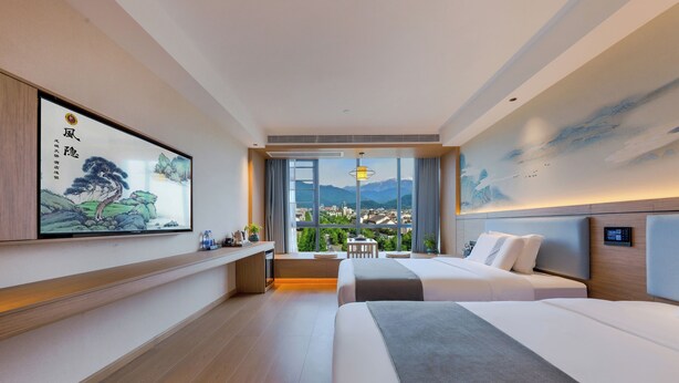 Ein modernes Hotelzimmer mit zwei Betten, einem Schreibtisch und einem großen Fenster mit Blick auf die Stadt.