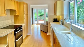 Een moderne keuken met houten kasten, een ingebouwde oven, een groot raam met uitzicht op groen en een schuifdeur naar een balkon.
