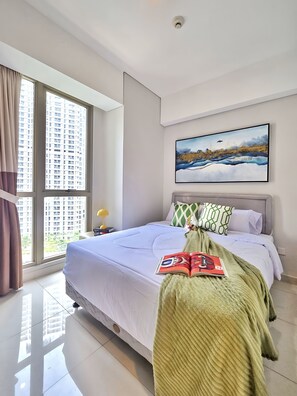 Une chambre d’hôtel avec un grand lit, une fenêtre avec des rideaux, un tableau au mur et un livre sur le lit.
