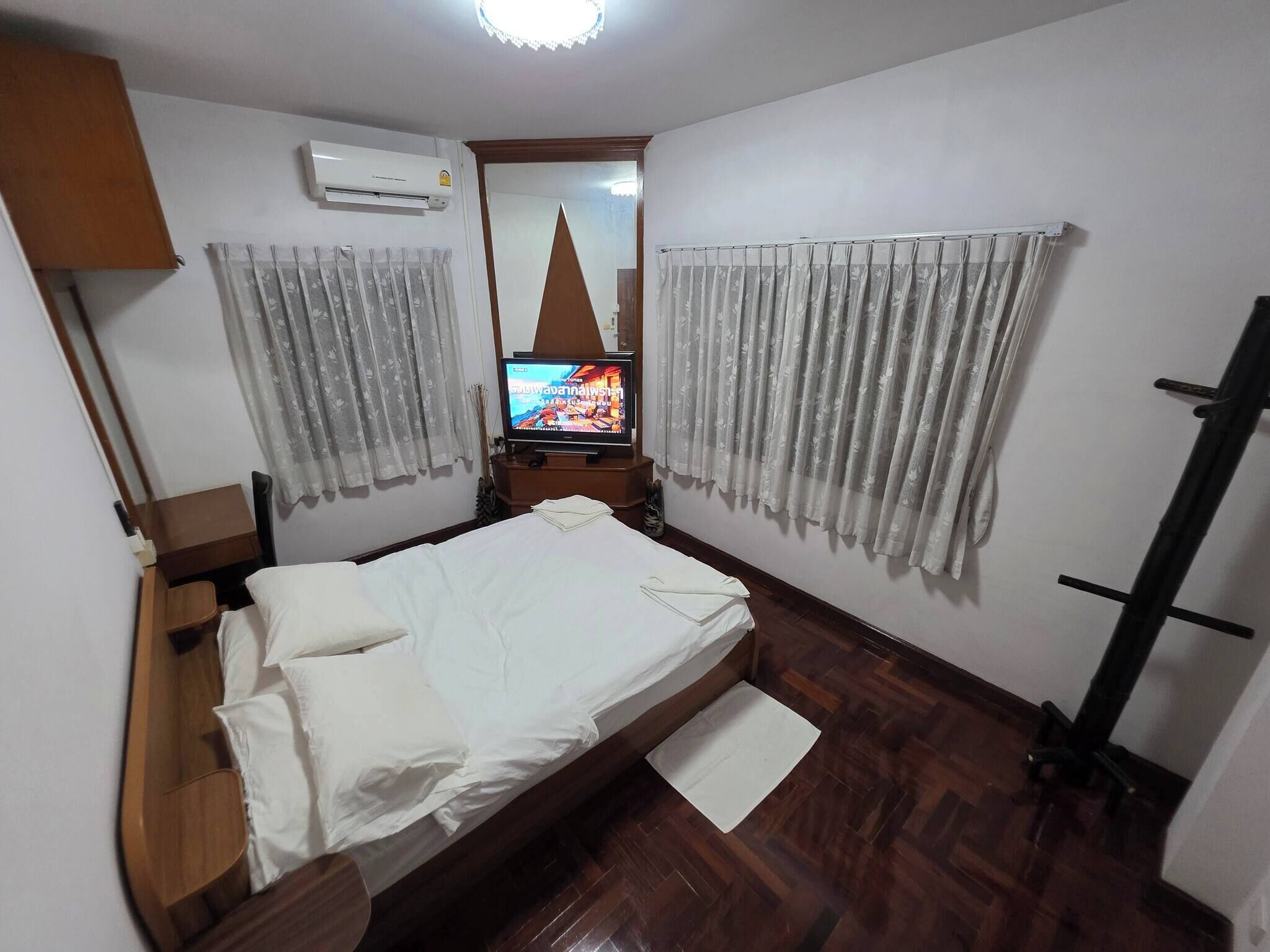 A small, neatly arranged bedroom with a bed, a TV, curtains, and an air conditioning unit.