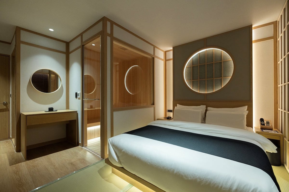 A modern hotel room with a bed, bedside table, and a large circular window.