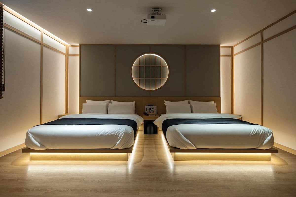 A hotel room with two beds, a large circular window, and a projector on the ceiling.