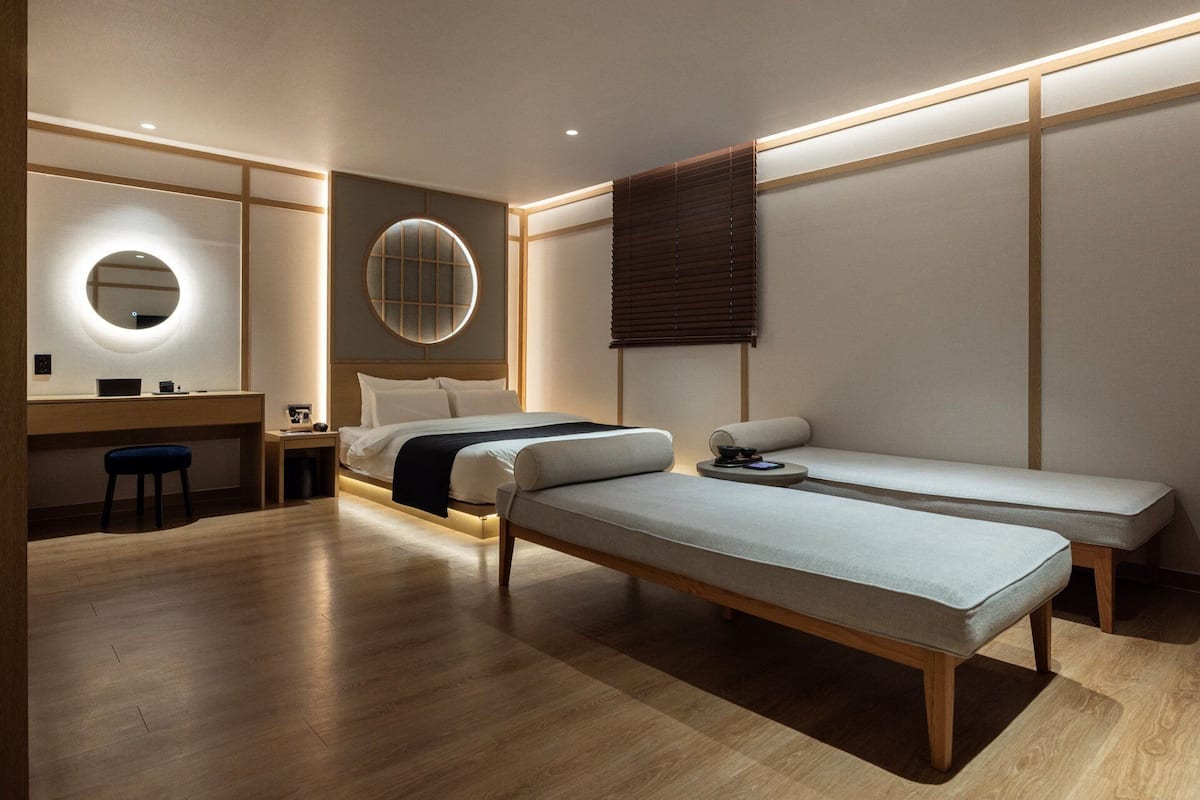 A modern hotel room with a bed, a desk, a chair, and a small seating area.