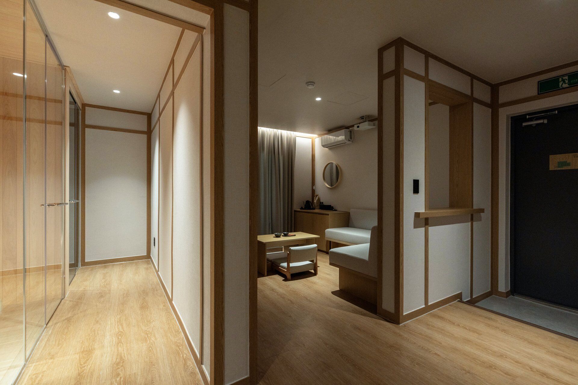 A hotel room with a wooden floor, a bed, a desk with a chair, and a small table with a chair.