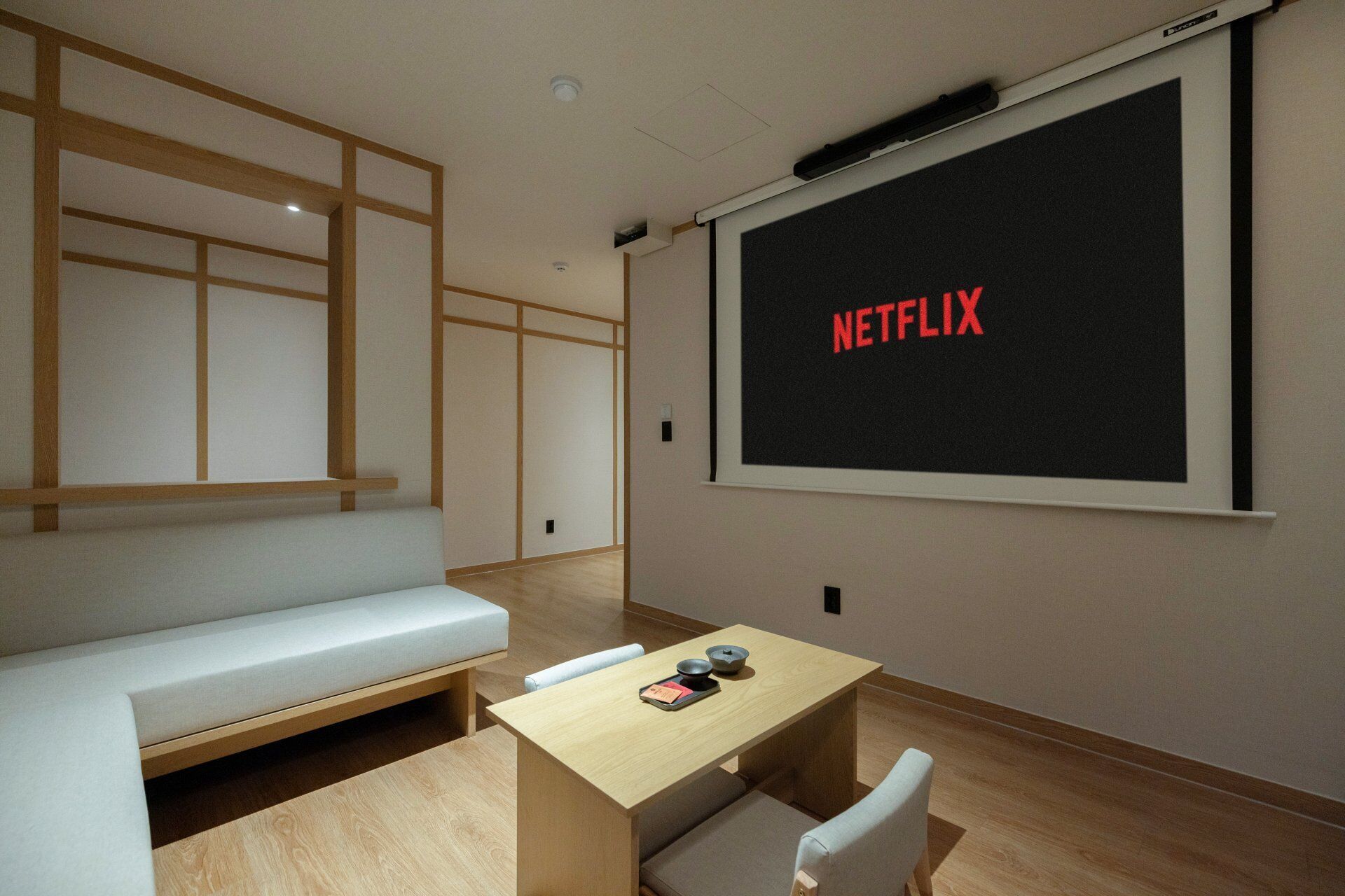 Una habitación con una pantalla grande mostrando 'NETFLIX', una mesa de madera con una bandeja, un banco y una pared con diseño de paneles de madera.