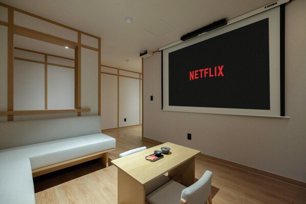 Una habitación con una pantalla grande mostrando 'NETFLIX', una mesa de madera con una bandeja, un banco y una pared con diseño de paneles de madera.