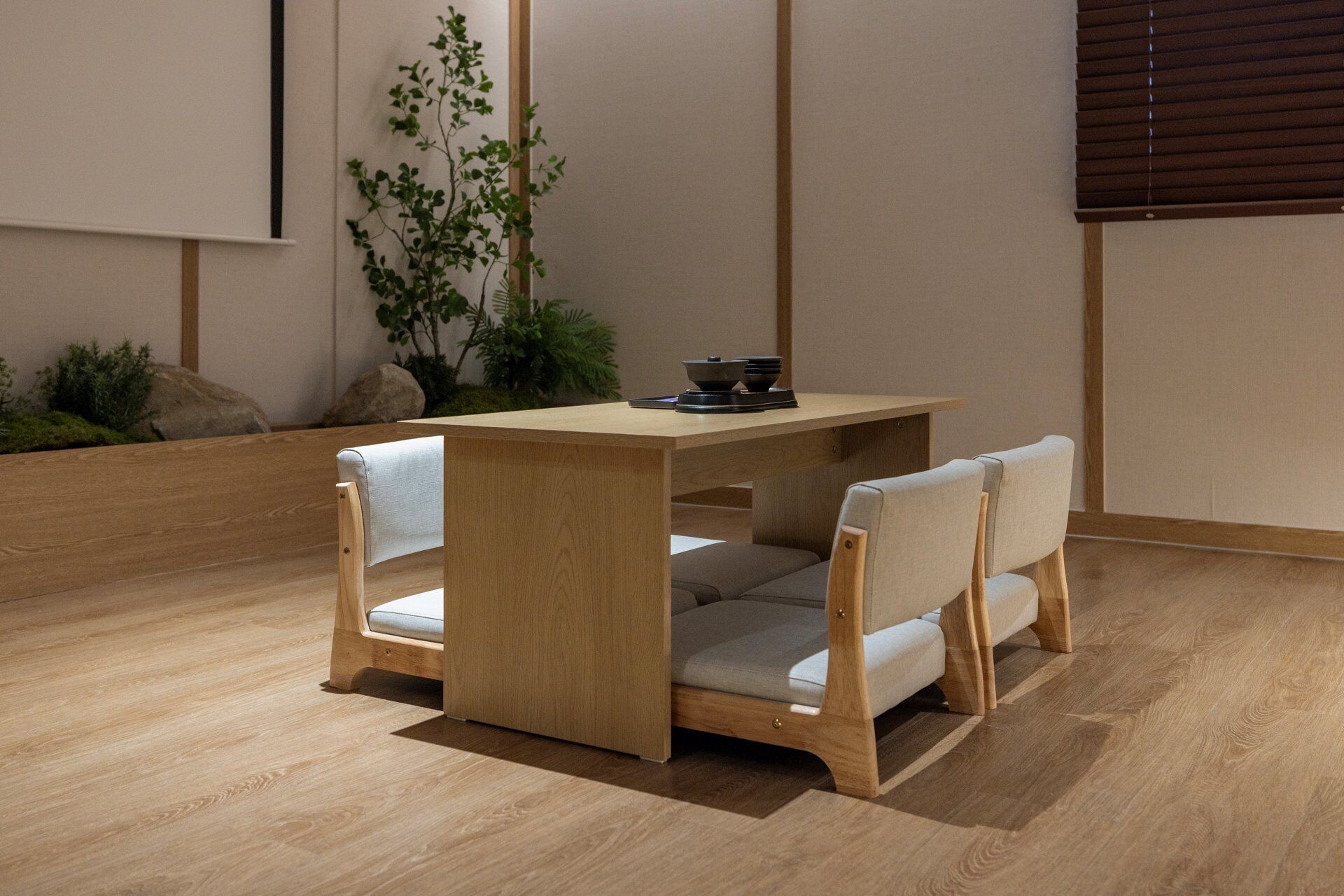 A wooden dining table with two chairs, a small plant, and a window with blinds.