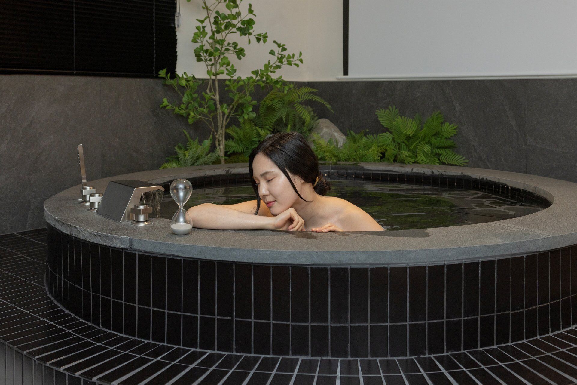 A woman relaxing in a hot tub with a modern design, surrounded by greenery.