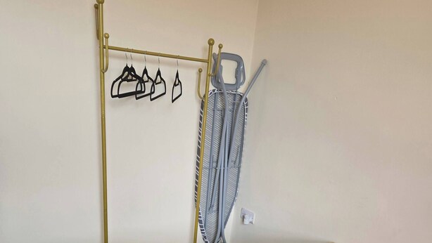 A room with a bed, a metal drying rack, and a chair. - Glams 2beds Luxury Stylish Apartment (Wolverhampton)