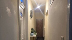 A narrow hallway with a carpeted floor, a small table with a plant, and a door with a window. - Glams 2beds Luxury Stylish Apartment (Wolverhampton)