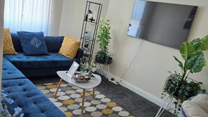 A living room with a blue sofa, a coffee table, a TV, and a clock on the wall. - Glams 2beds Luxury Stylish Apartment (Wolverhampton)