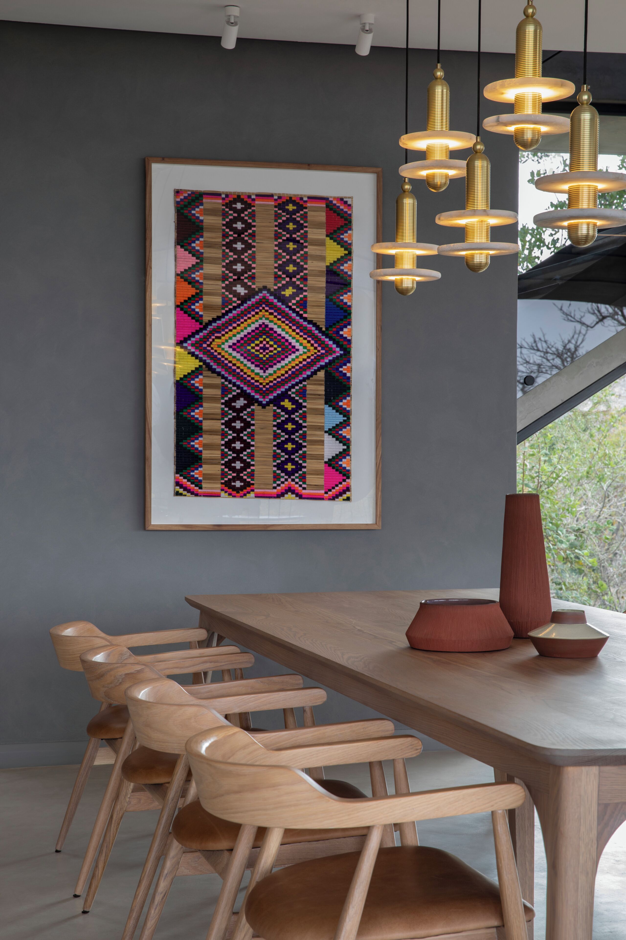 A dining area with a wooden table and chairs, a colorful abstract painting on the wall, and a modern pendant light fixture.