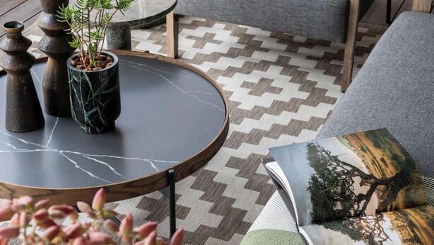 Un espacio exterior moderno con una mesa redonda, dos sillas y un centro decorativo con plantas.