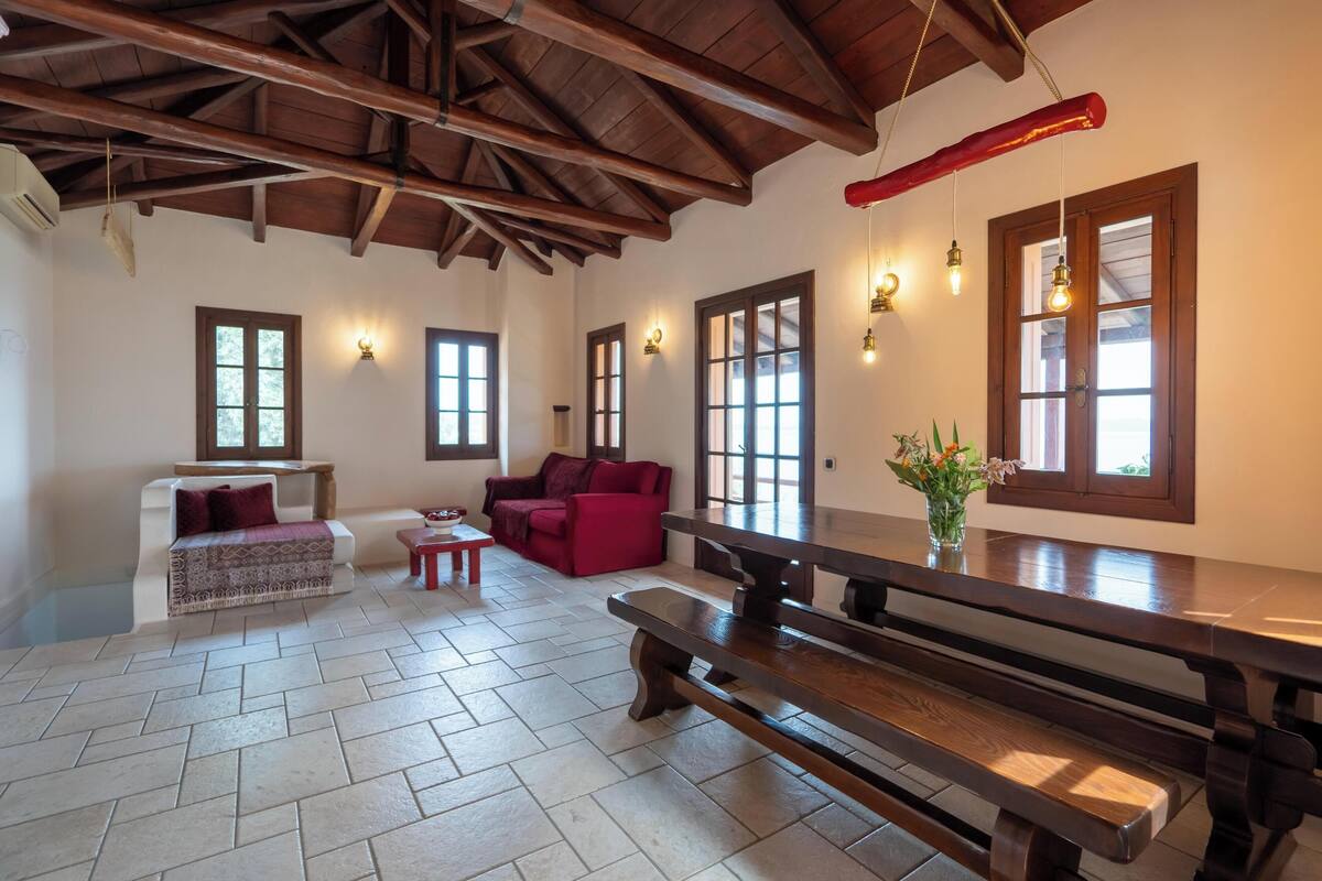 A spacious room with a wooden ceiling, a large wooden bench, a white sofa, a red sofa, and a small table.