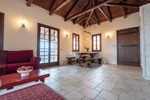 Un salón acogedor con un sofá rojo, una mesa de centro de madera con manzanas, suelo de baldosas de piedra y techo de madera.