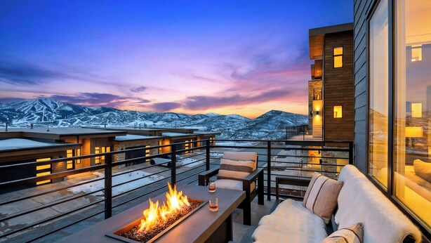 Un'area salotto esterna moderna con un elemento decorativo a fuoco, con vista su un paesaggio montano innevato.