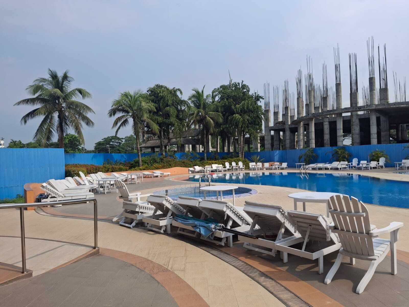 A pool area with lounge chairs, palm trees, and a modern building structure in the background.