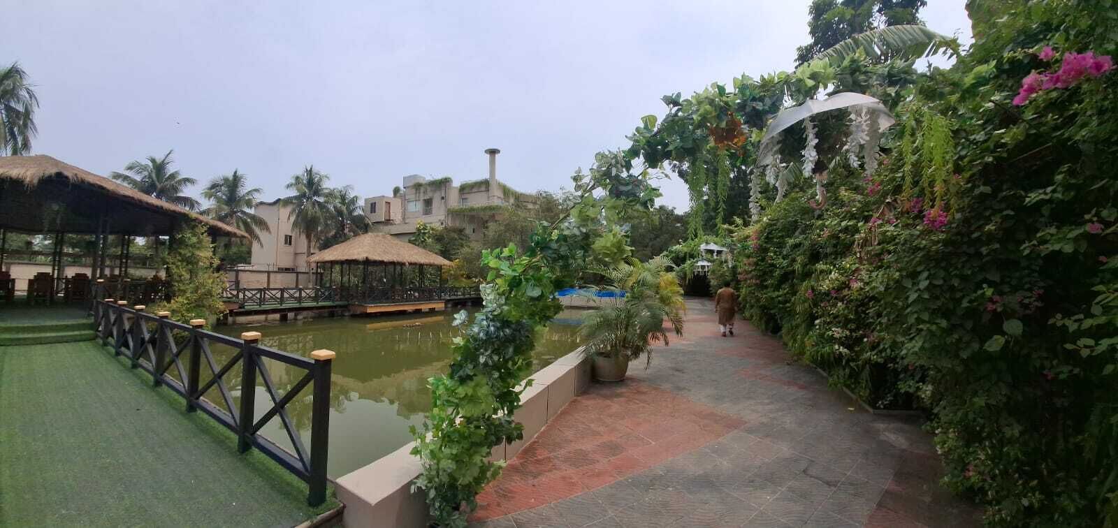 Un espace jardin agrémenté d’un élément aquatique, d’une structure à toit de chaume et d’une végétation luxuriante.