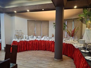 Une salle de banquet avec une table incurvée recouverte d’une nappe rouge, entourée de chaises et d’un grand pilier.