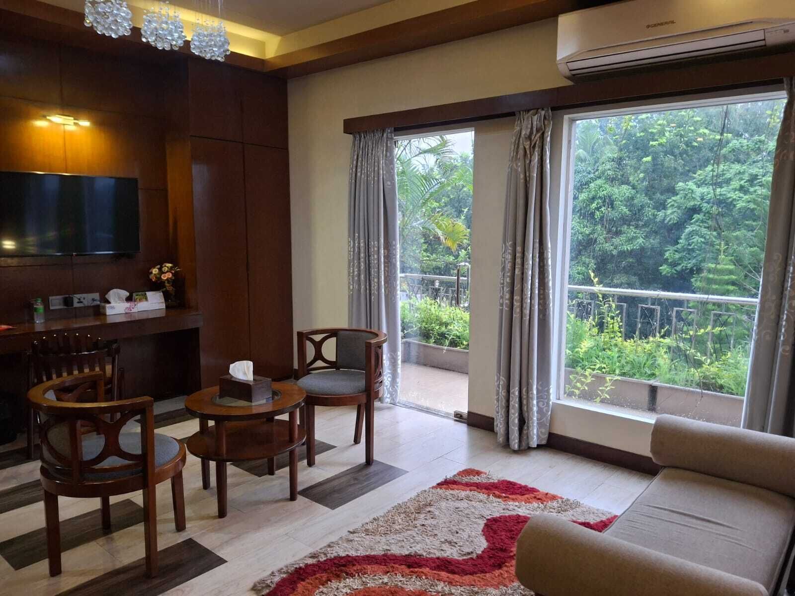 Sala de estar con un sofá, dos sillones, una mesita, televisor y balcón con vistas a zonas verdes.
