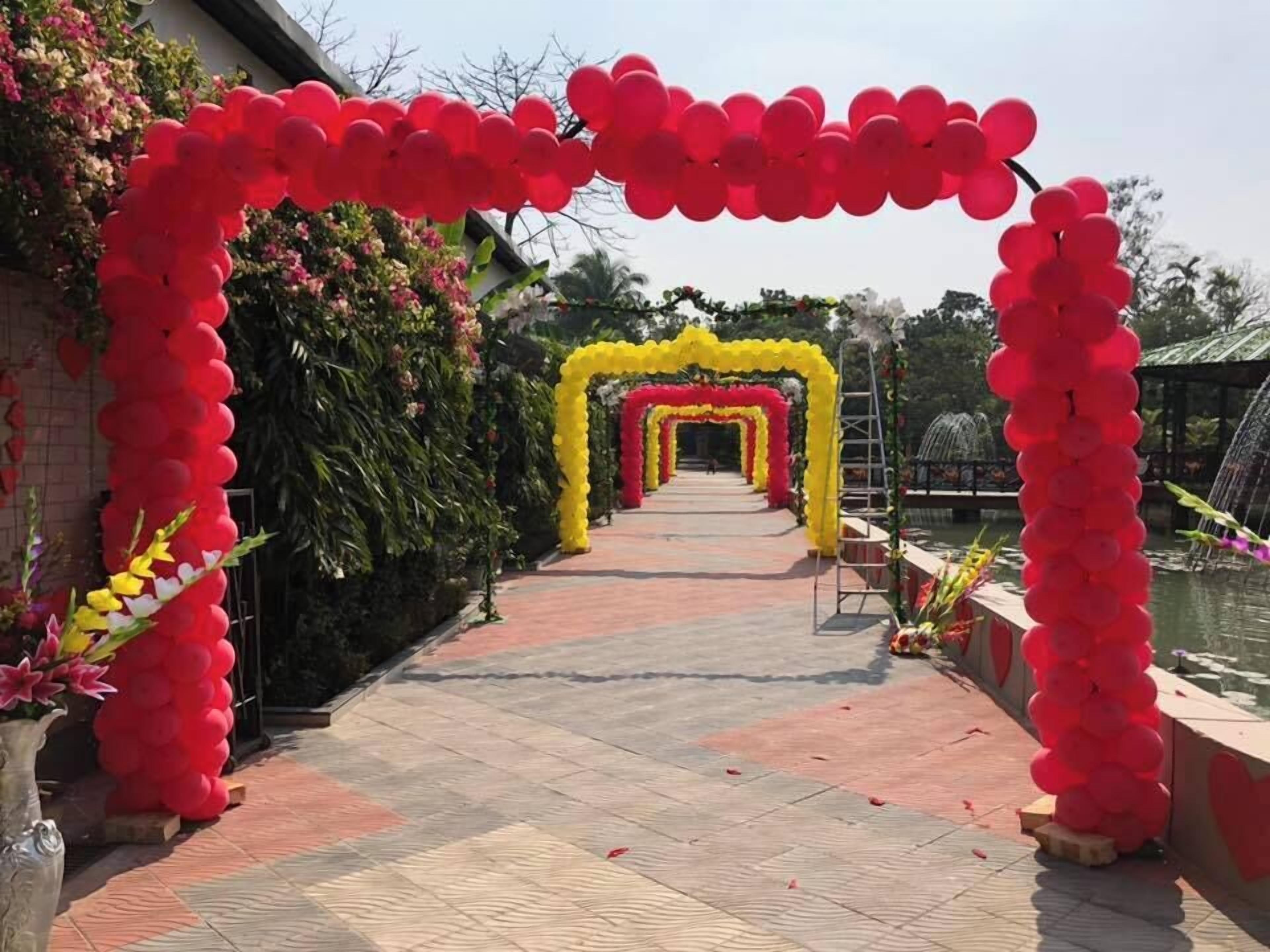 Un chemin bordé d’une arche décorée de ballons rouges et jaunes, qui mène à un bâtiment.