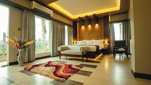 Une chambre d’hôtel moderne dotée d’un grand lit, d’un coin salon, d’un bureau et offrant une vue sur la verdure environnante.