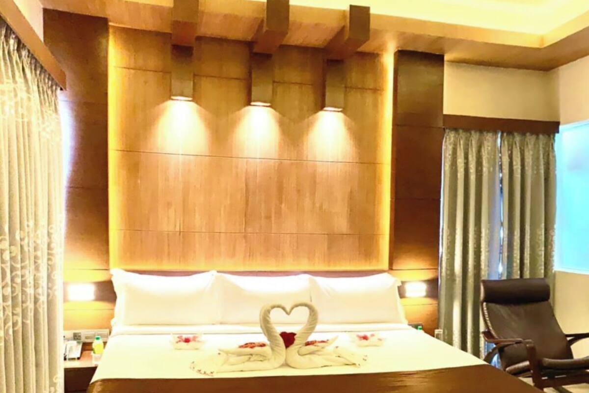 Ett hotellrum med en stor säng, en sänggavel i trä och en handduksdekoration formad som ett hjärta.