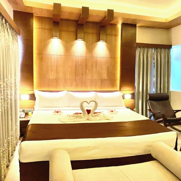 Une chambre d’hôtel avec un grand lit, une tête de lit en bois et une décoration en forme de cœur réalisée avec des serviettes.