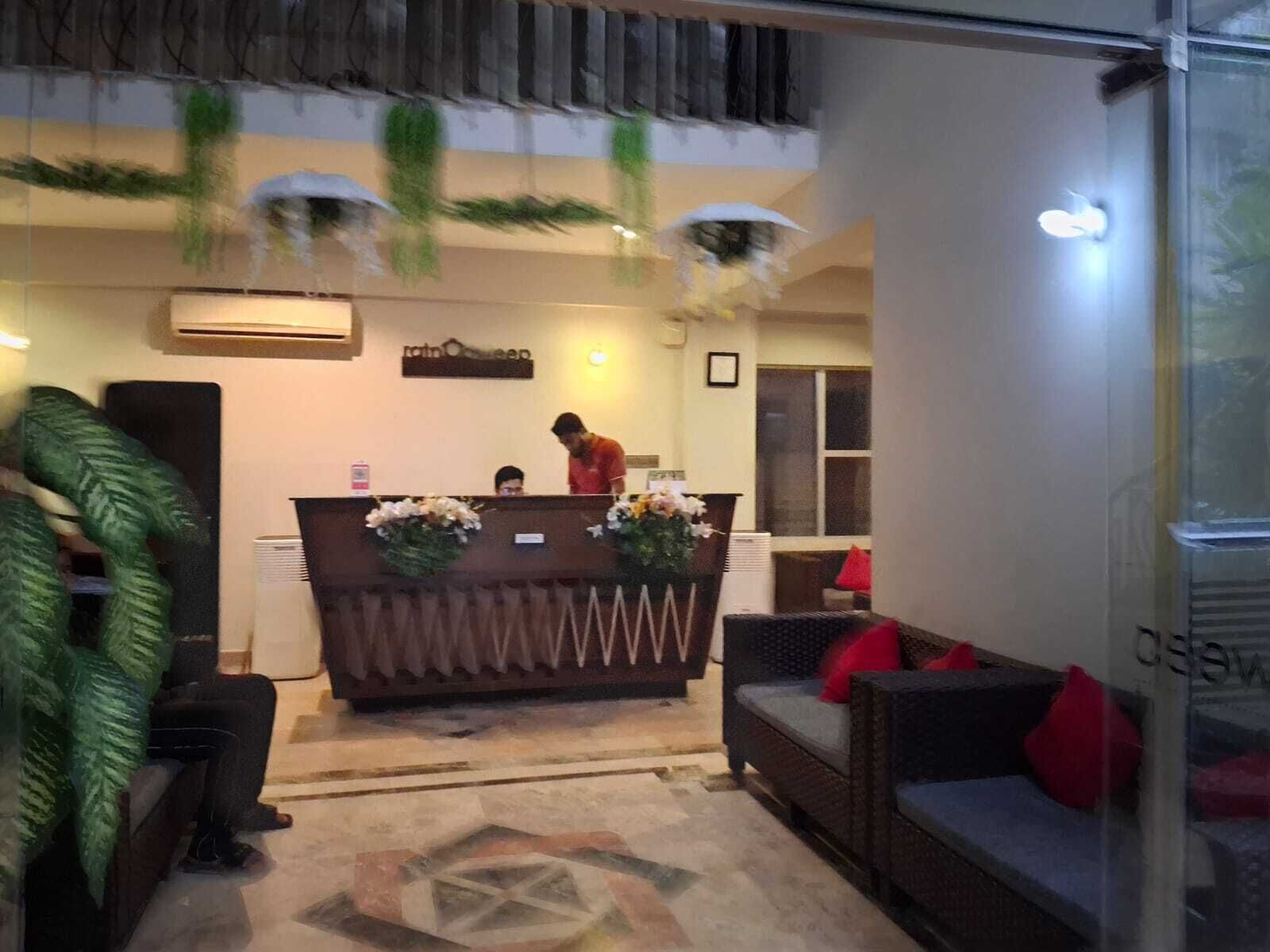 A reception area with a counter, a receptionist, and a sofa with red cushions.