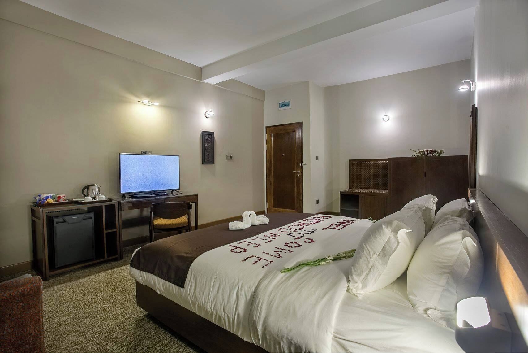 A hotel room with a bed, a desk with a computer, a television, and a minibar.