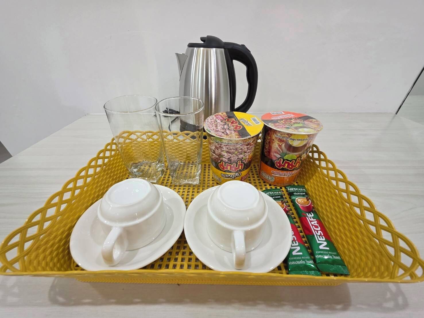Una bandeja con dos tazas blancas, dos vasos, una tetera y dos recipientes de café instantáneo.