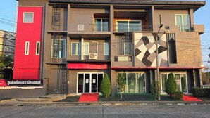 Un immeuble à plusieurs étages, doté d’une façade rouge et grise, de grandes fenêtres et d’un motif géométrique sur le côté droit.
