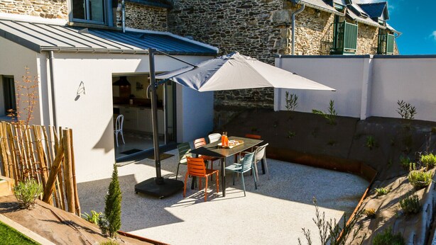 A modern house with a stone facade, a patio with a table and chairs, and a large umbrella. - Azur Cancale (Cancale)