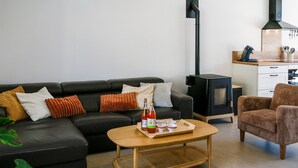 A living room with a sofa, a coffee table, a chair, a fireplace, and a kitchen area. - Azur Cancale (Cancale)