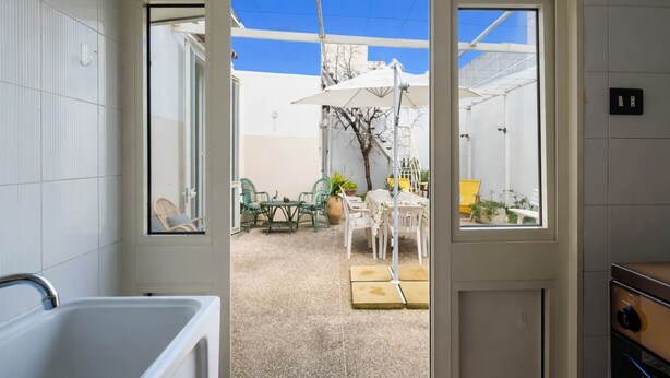 Une salle de bain avec un lavabo blanc et une vue sur un patio extérieur aménagé avec une table, des chaises et des parasols.