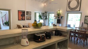 A modern kitchen with a central island, a coffee maker, a toaster, and a blender. There are plants and a fruit bowl on the island. - Leonora House, Talpe (Galle)