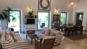 A spacious living room with striped sofas, a coffee table, a TV, and a dining area with wooden chairs and a table. - Leonora House, Talpe (Galle)