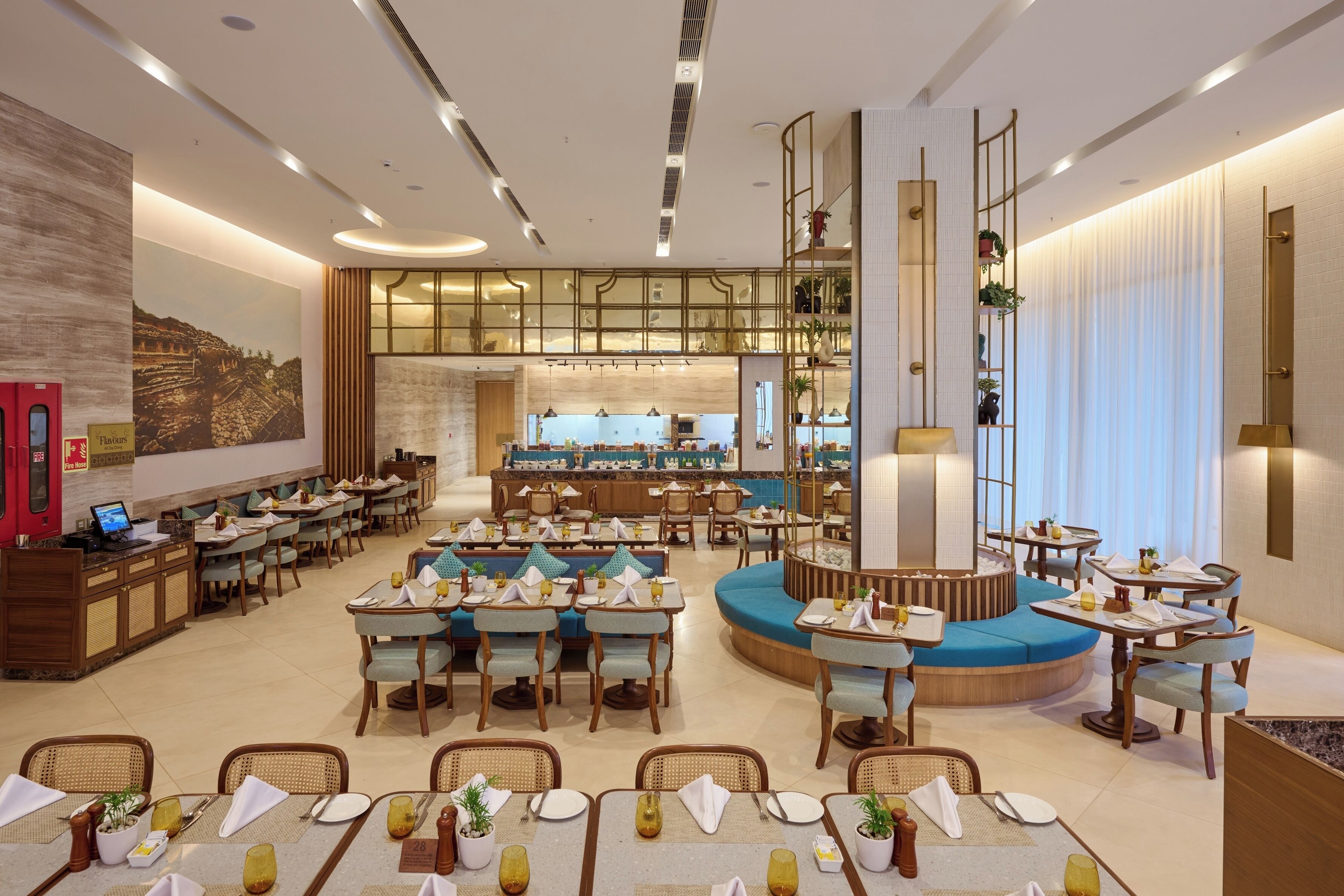 Un amplio comedor de hotel con diversas opciones de asientos, una barra central y vistas a la cocina.
