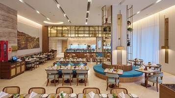 Un amplio comedor de hotel con diversas opciones de asientos, una barra central y vistas a la cocina.