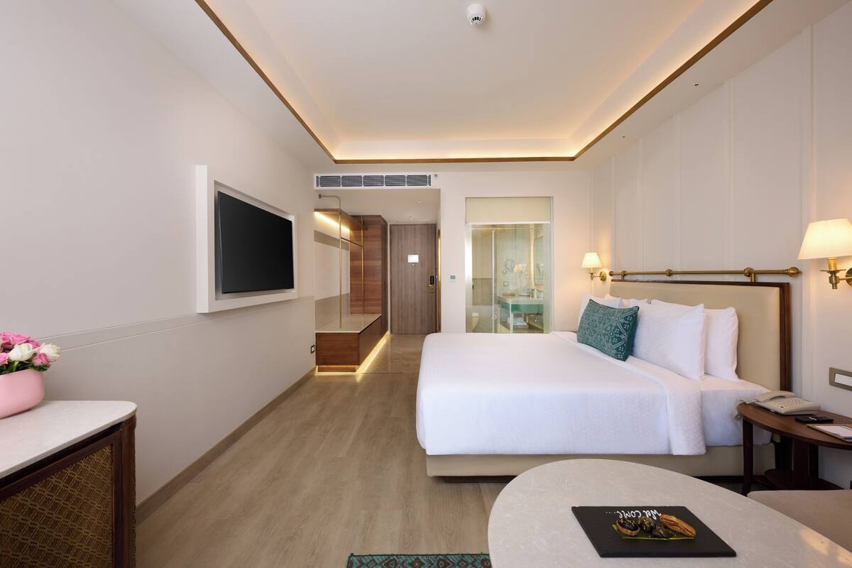 Habitación de hotel con cama, mesita de noche, lámpara, televisor y una pequeña mesa con un menú.