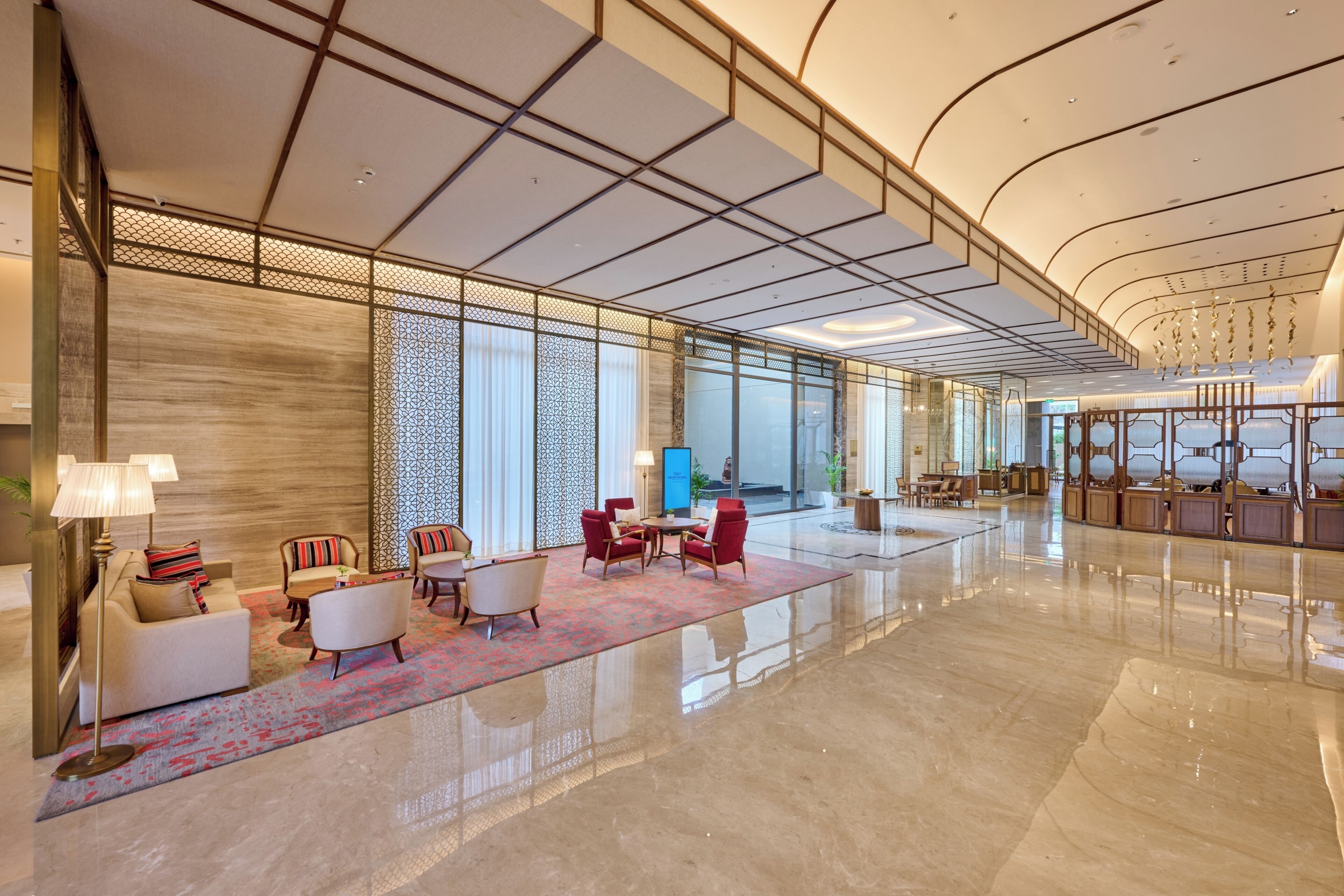Un hall d’entrée spacieux avec un sol ciré, un coin salon comprenant des fauteuils et un canapé, un mur décoré de motifs et une grande fenêtre.