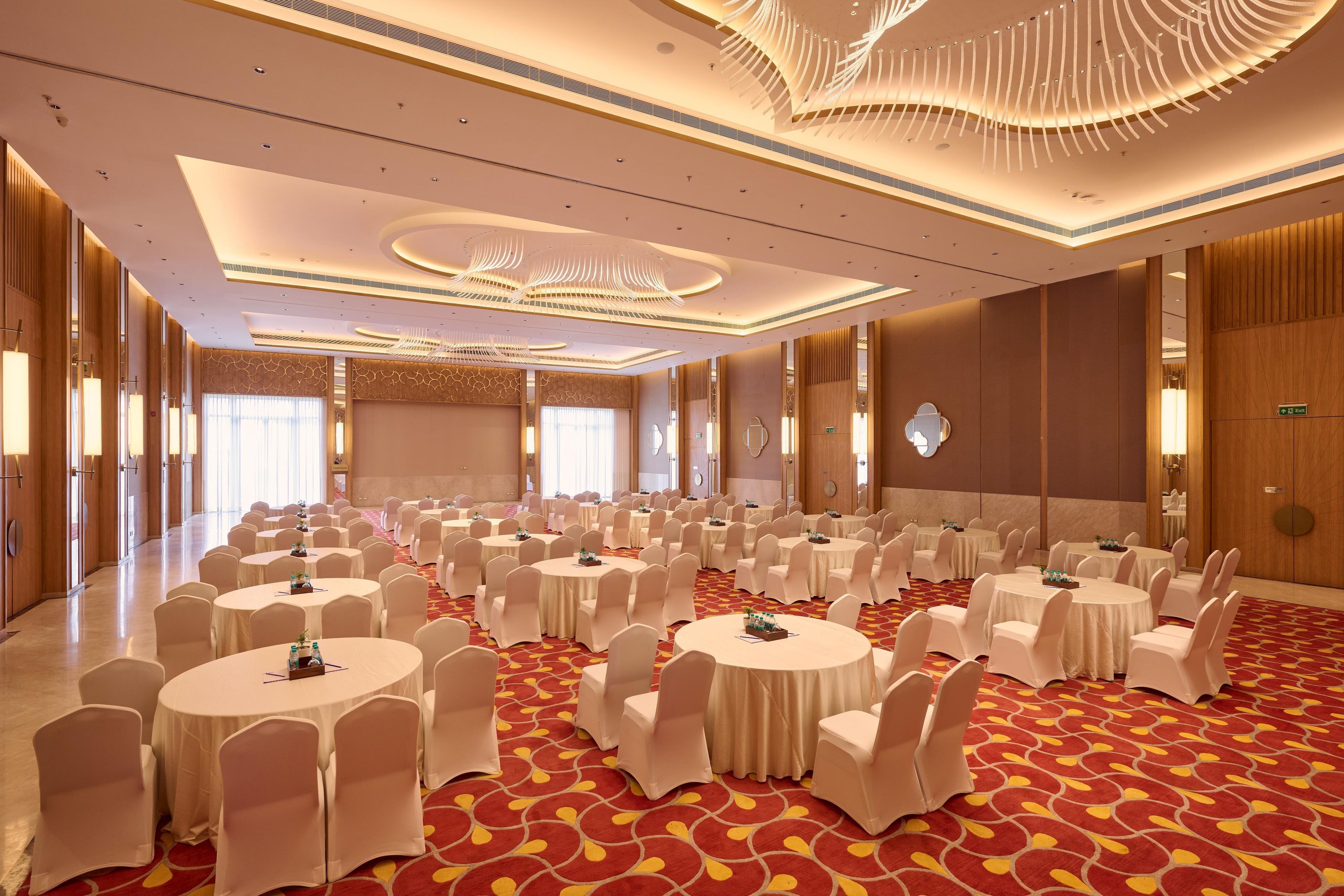 A conference room with multiple round tables, white chairs, and a red patterned carpet.