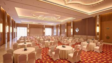 A conference room with multiple round tables, white chairs, and a red patterned carpet.