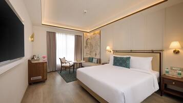 A hotel room with a large bed, a desk, a chair, a small table, and a TV.