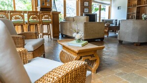 Un espace intérieur spacieux, aménagé avec des meubles en osier, une table basse en bois agrémentée d’un livre et de fleurs, et un téléviseur.