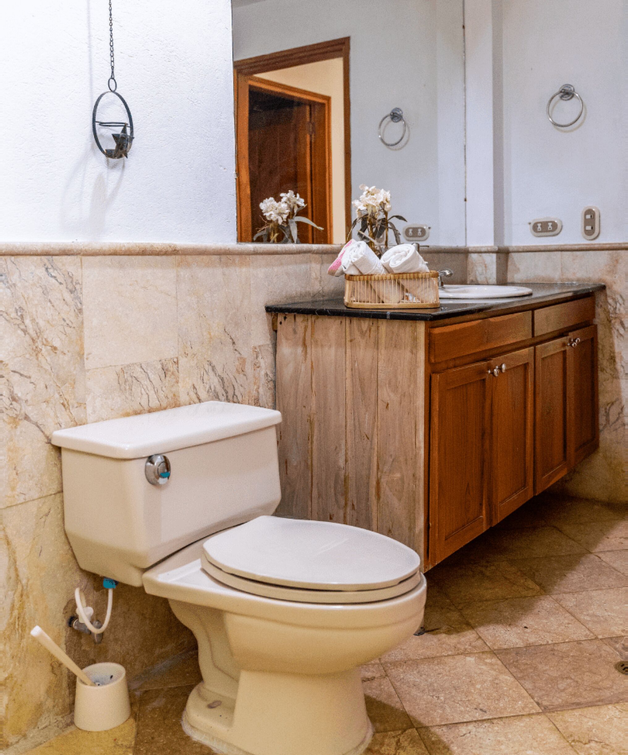 A bathroom with a toilet, wooden cabinets, a marble wall, and a small sink.