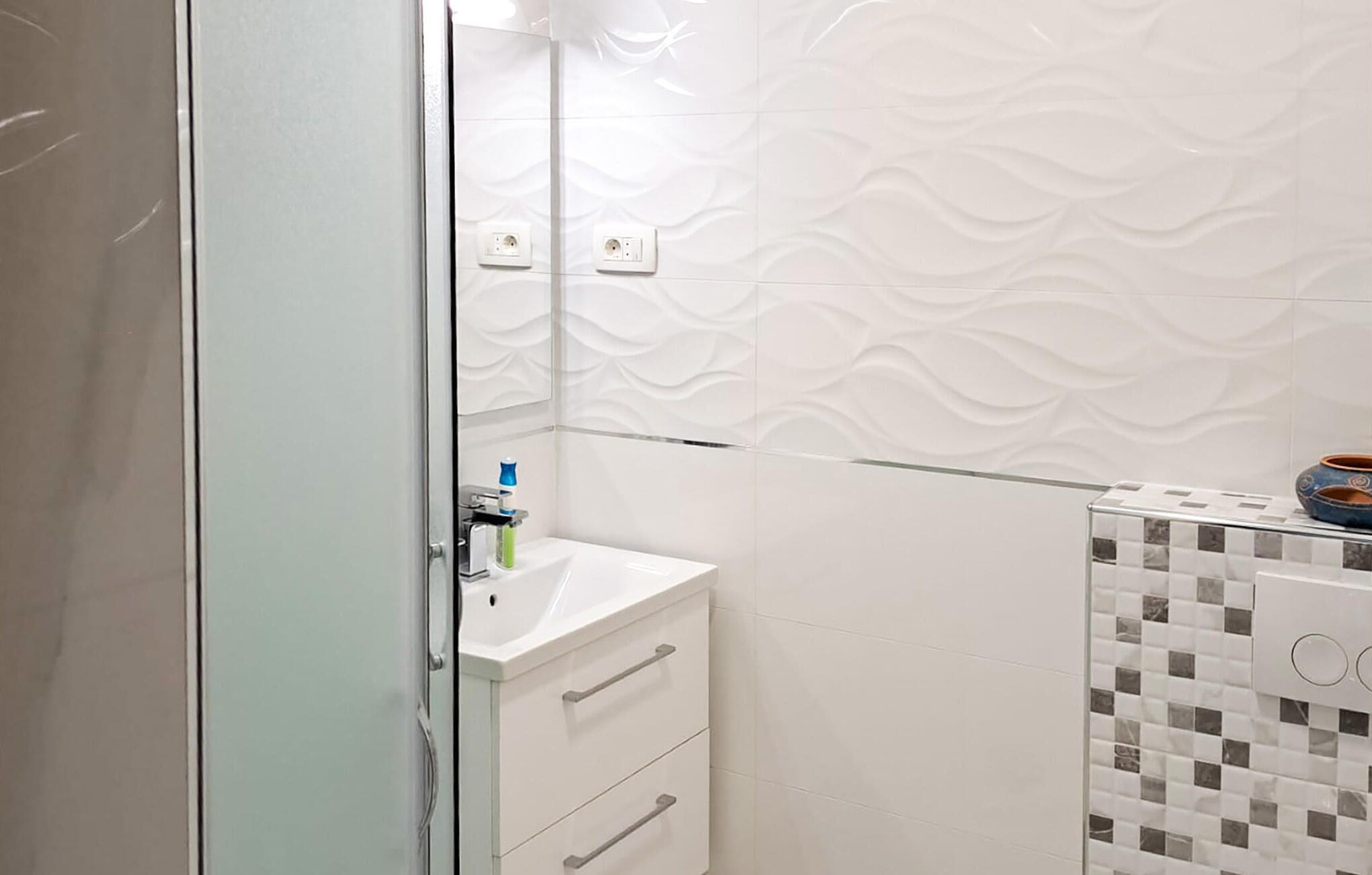 Un bany amb un lavabo blanc, un mirall i una paret amb un disseny decoratiu.