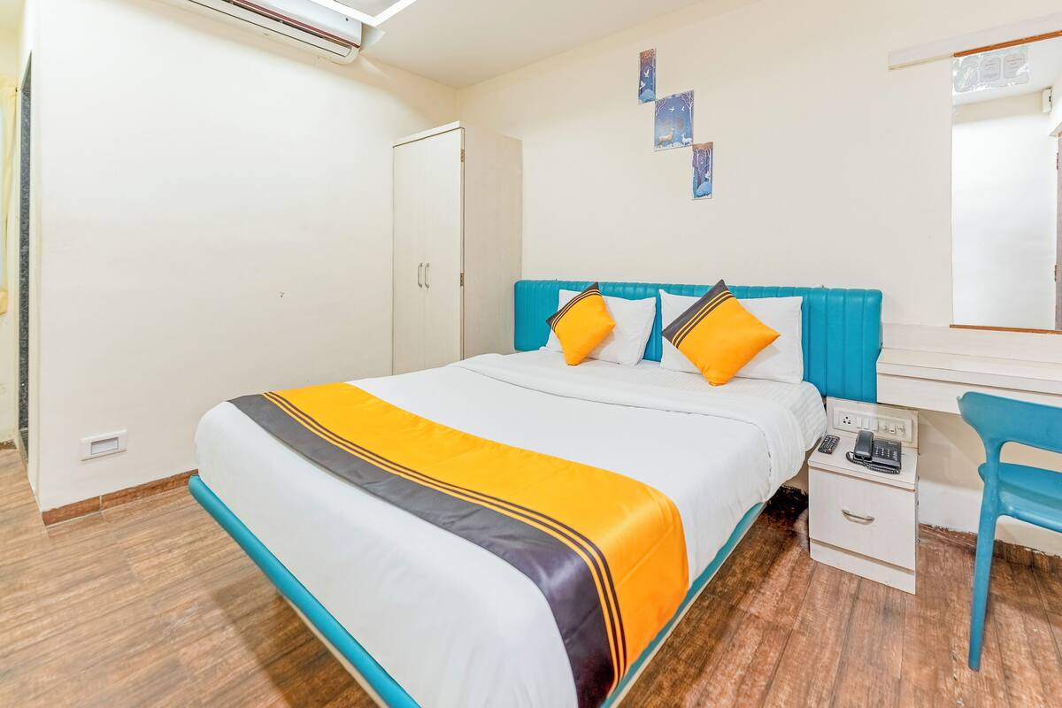 A hotel room with a bed, a desk, a chair, a wardrobe, and a mirror.