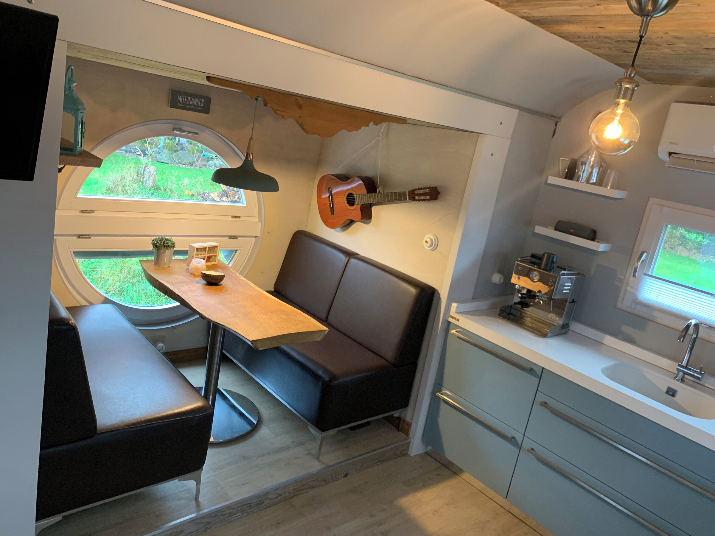 A compact kitchen with a dining area, a guitar, and a small window.